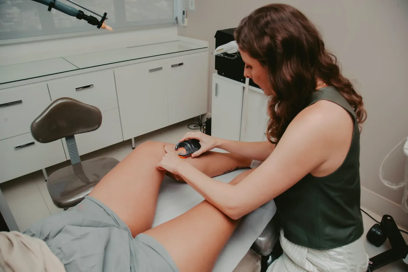 Dra. Milena aplicando laser transdérmico na perna de uma paciente